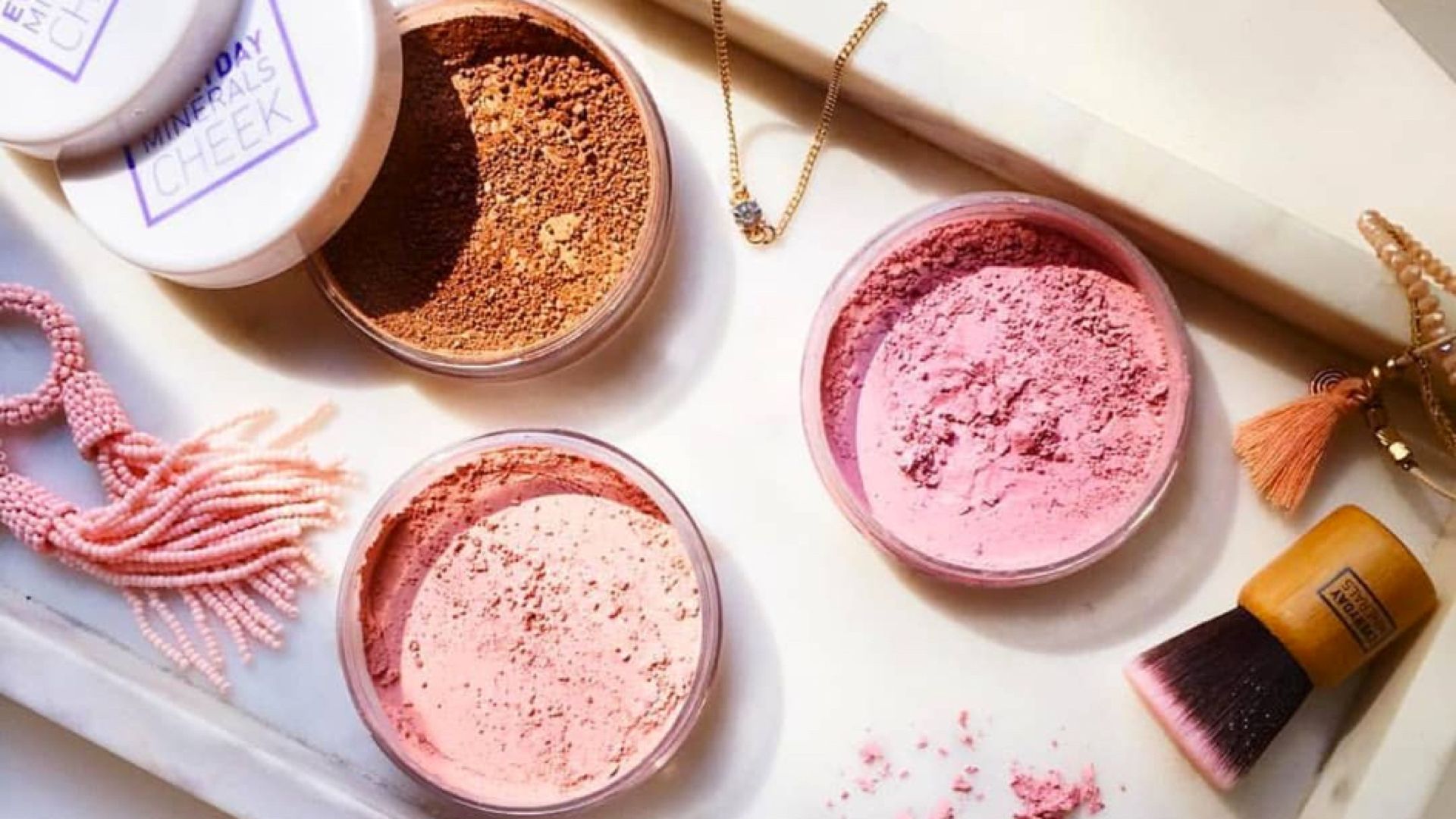 Loose Mineral Blush Powders in Pink and Bronze Shades with a Brush and Accessories on a Marble Tray.